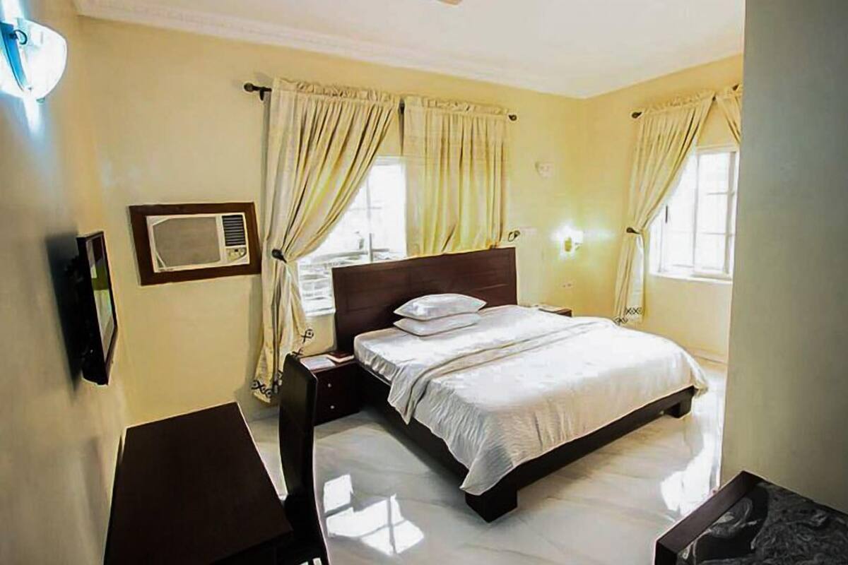 A hotel room with a bed, bedside table, lamp, and a window with curtains.