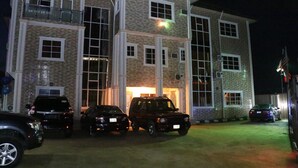 A multi-story building with a brick facade, large windows, and a balcony. There are several cars parked in front. - Carabana Hotel & Suites (Uyo)