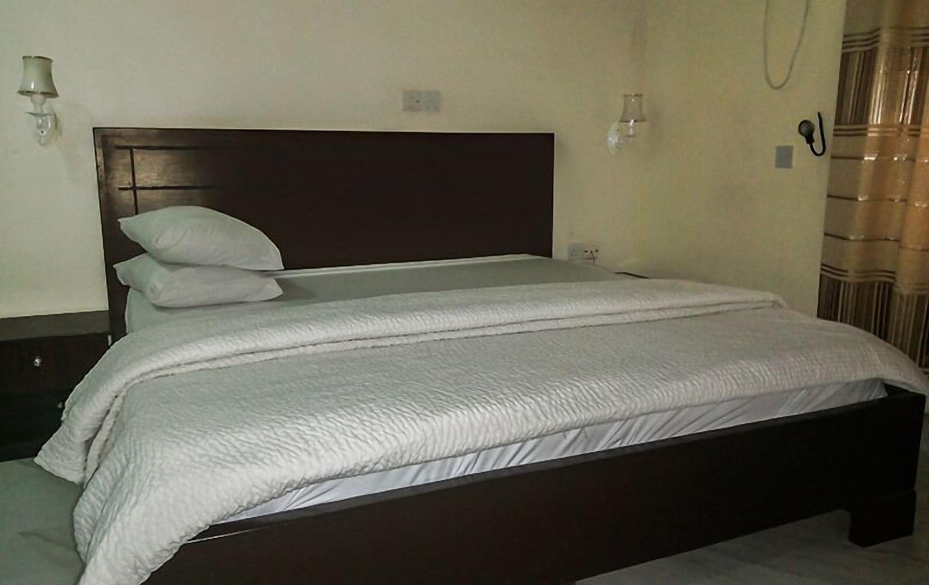 Una cama con cabecera oscura, ropa de cama blanca y una sola almohada.