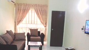 A living room with a sofa, armchair, and coffee table, a TV mounted on the wall, and a door. - Carabana Hotel & Suites (Uyo)