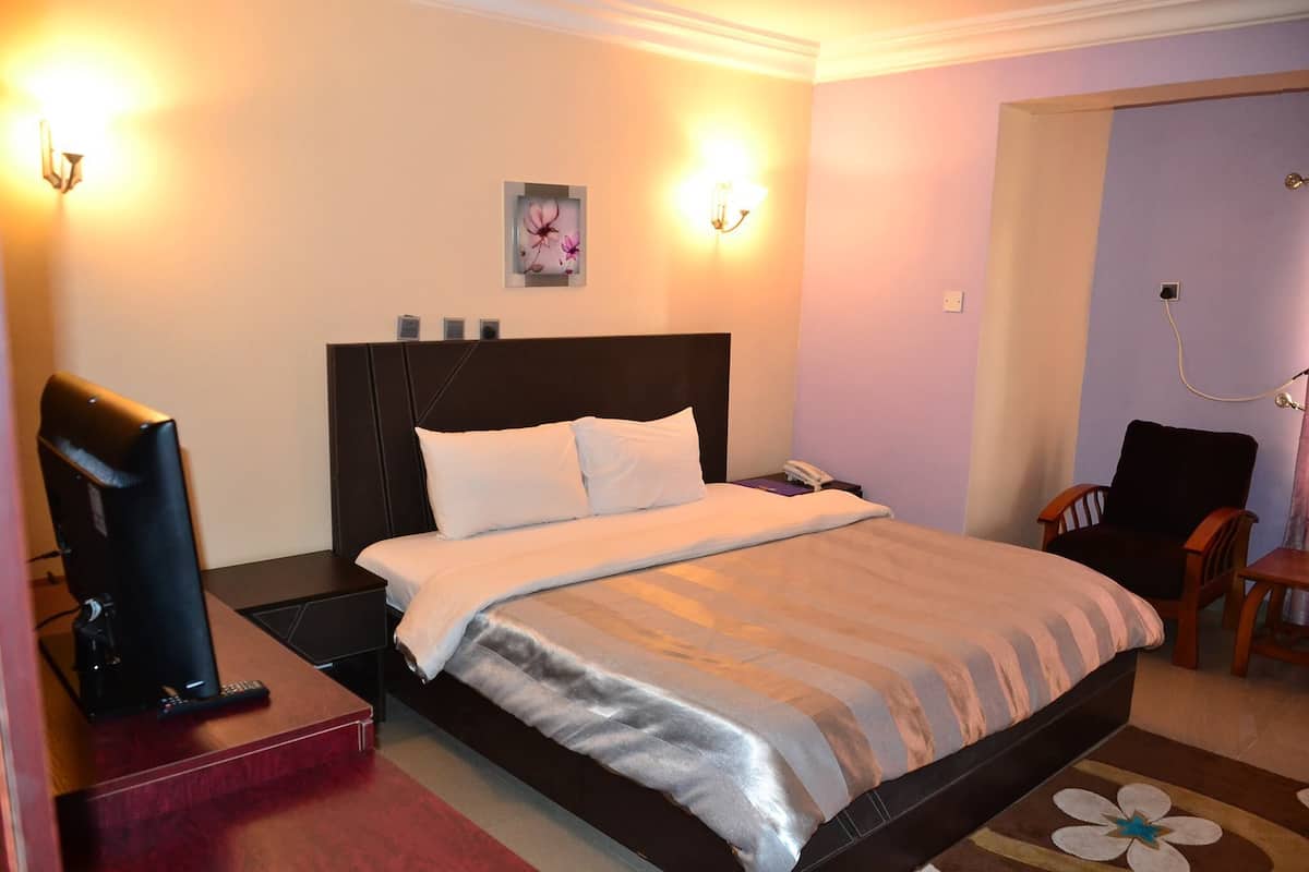 Une chambre d’hôtel bien rangée, avec un lit, une table de chevet, une télévision et une chaise.