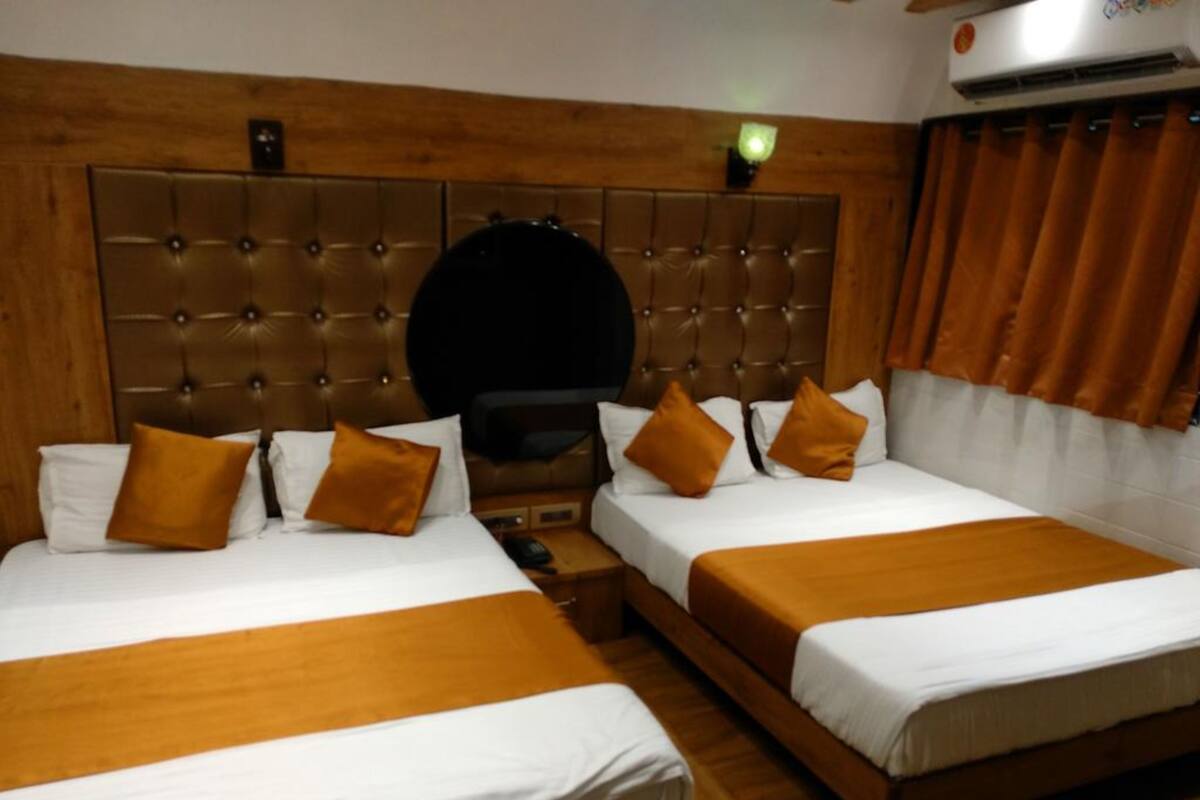 Une chambre d’hôtel avec deux lits, une tête de lit en bois, un téléviseur à écran plat et un appareil de climatisation.