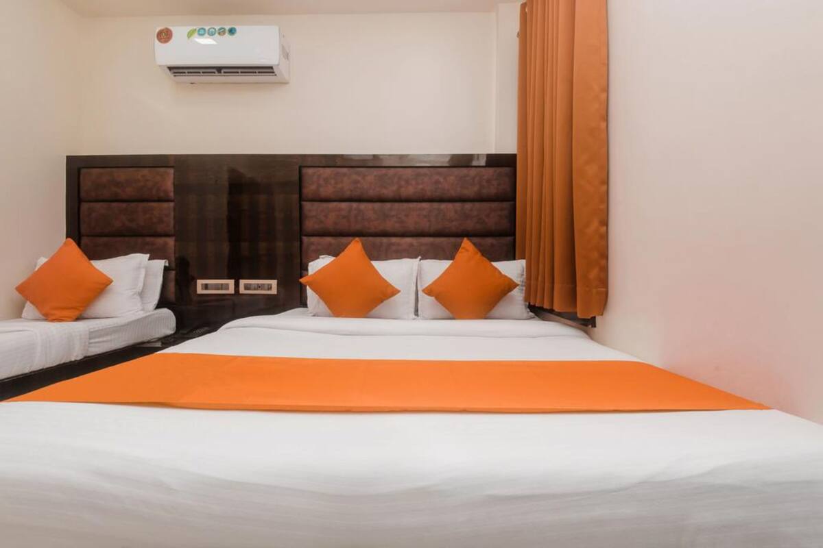 Une chambre d’hôtel avec un grand lit, deux petits lits et une tête de lit dotée d’un panneau de commande.