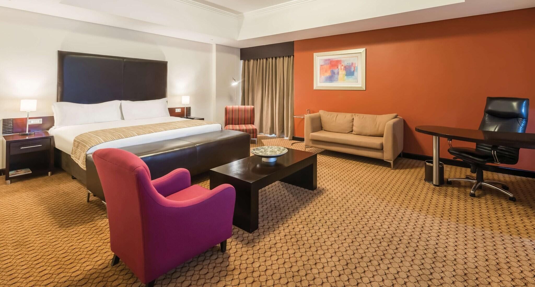 A hotel room with a bed, a sofa, a coffee table, a desk, and a chair.