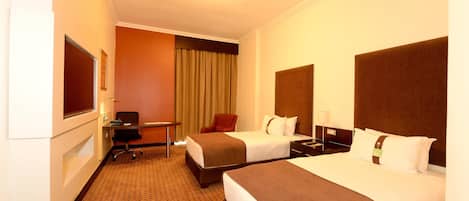 A hotel room with two beds, a desk, a chair, and a television.