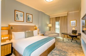 A hotel room with a large bed, a desk with a chair, a sofa, and two framed artworks on the wall. - Southern Sun Sandton (Johannesburg)