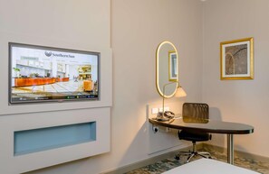 A hotel room with a mounted TV displaying the Southern Sun brand, a desk with a lamp, a chair, and a framed picture on the wall. - Southern Sun Sandton (Johannesburg)