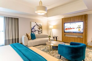 A hotel room with a bed, a sofa, a TV, a lamp, and a small table. - Southern Sun Sandton (Johannesburg)