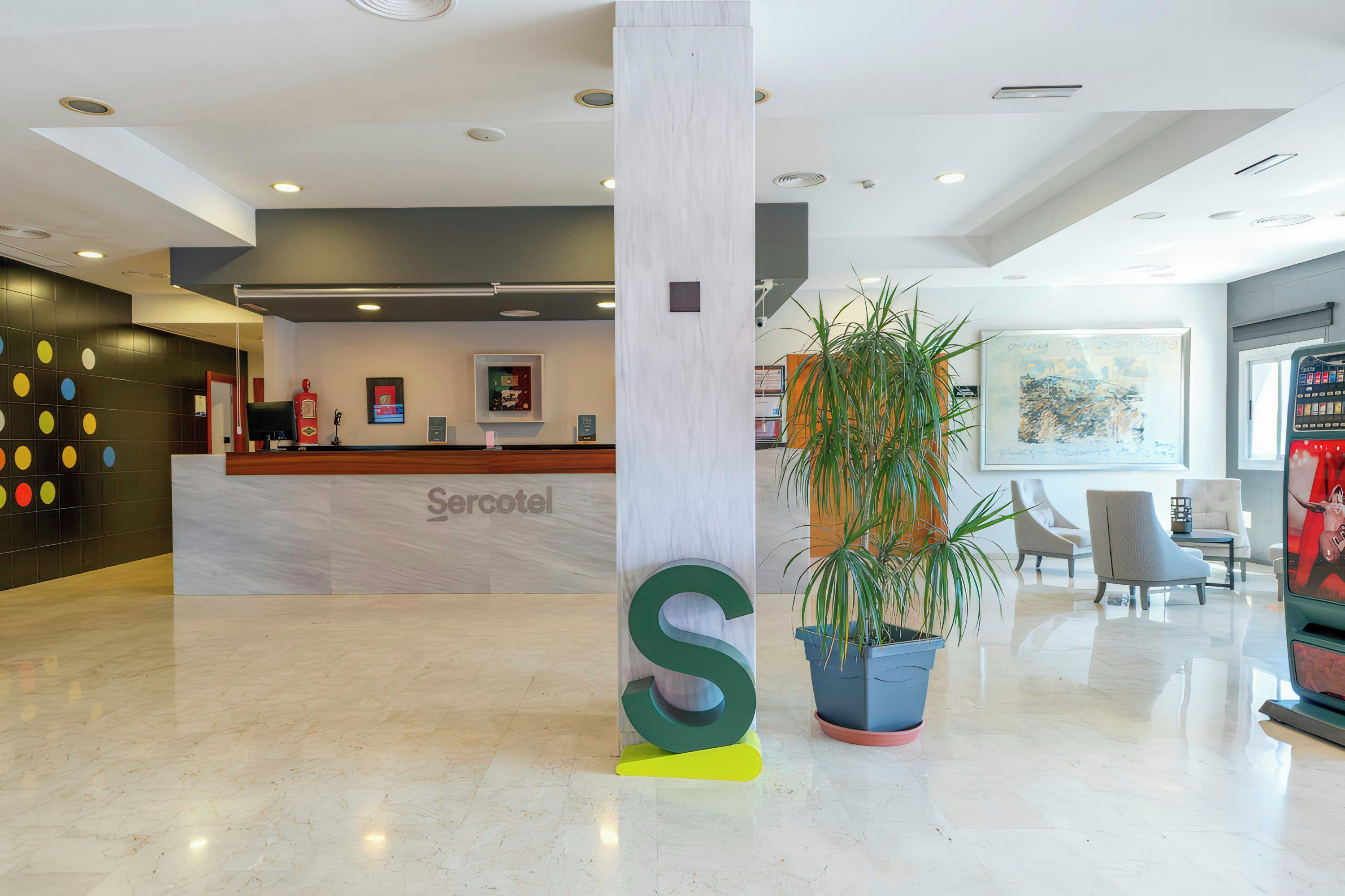 Un hall d'hôtel avec un sol en marbre, un comptoir d'accueil portant l'inscription « Sercotel » et une grande colonne sur laquelle est gravée la lettre « S ».