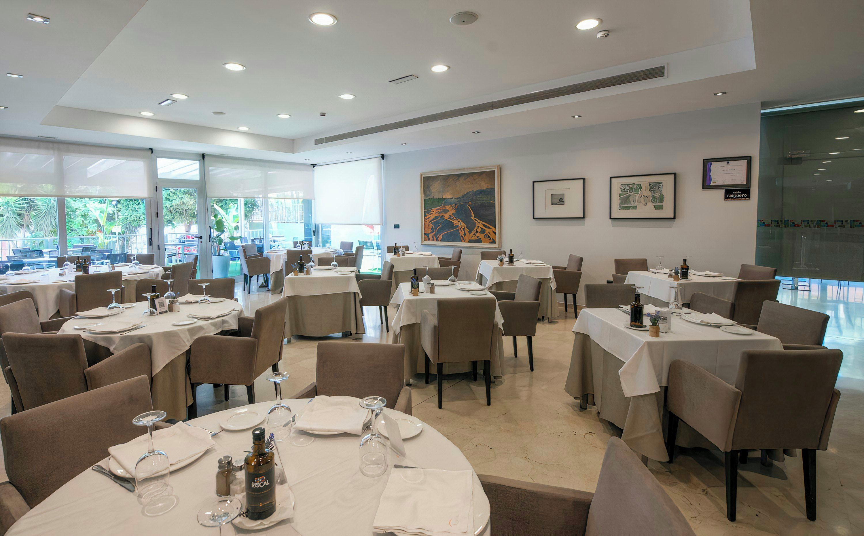 Un restaurante con mesas redondas, sillas y vistas al exterior.