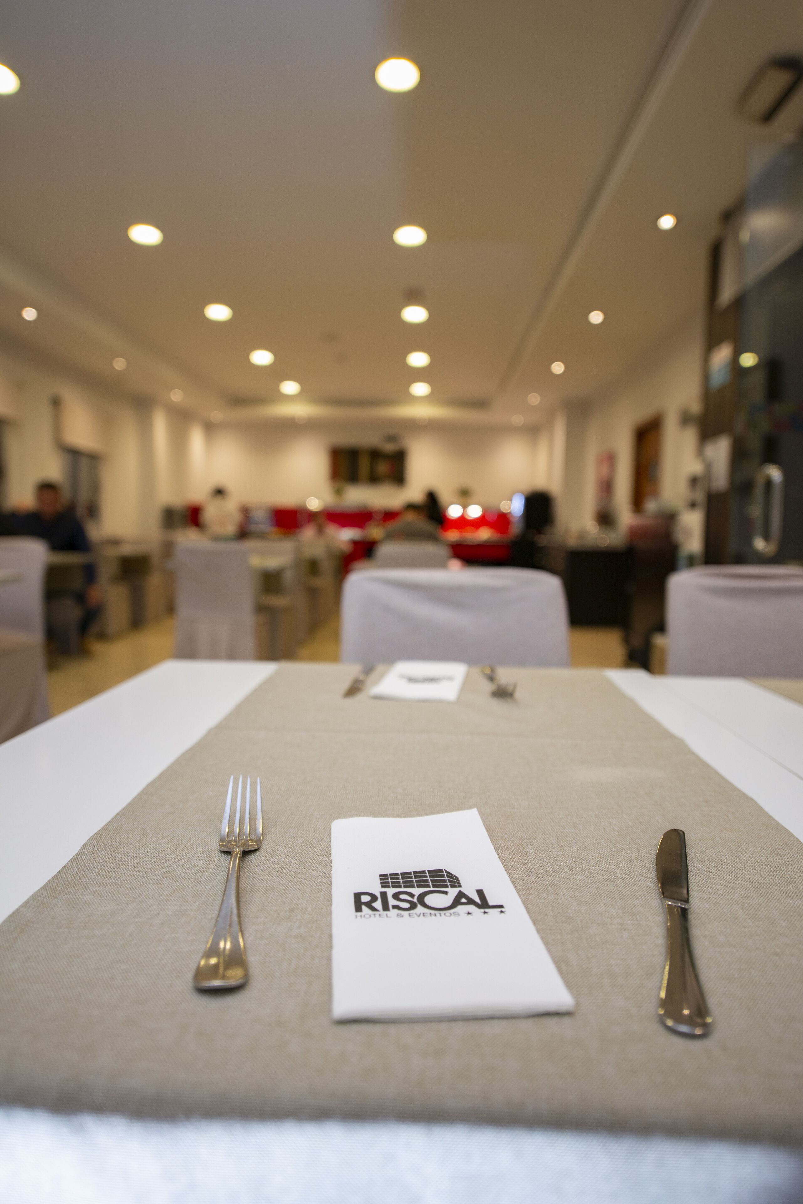 Un comedor de hotel con mesas dispuestas para una comida, un menú y un logotipo en el mantel.