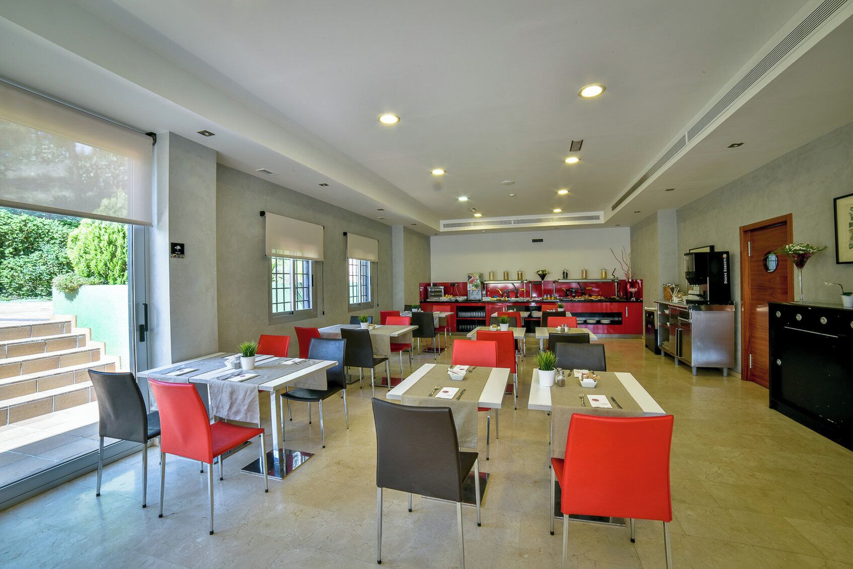 A spacious dining area with multiple tables and chairs, a kitchen in the background, and a staircase leading outside.