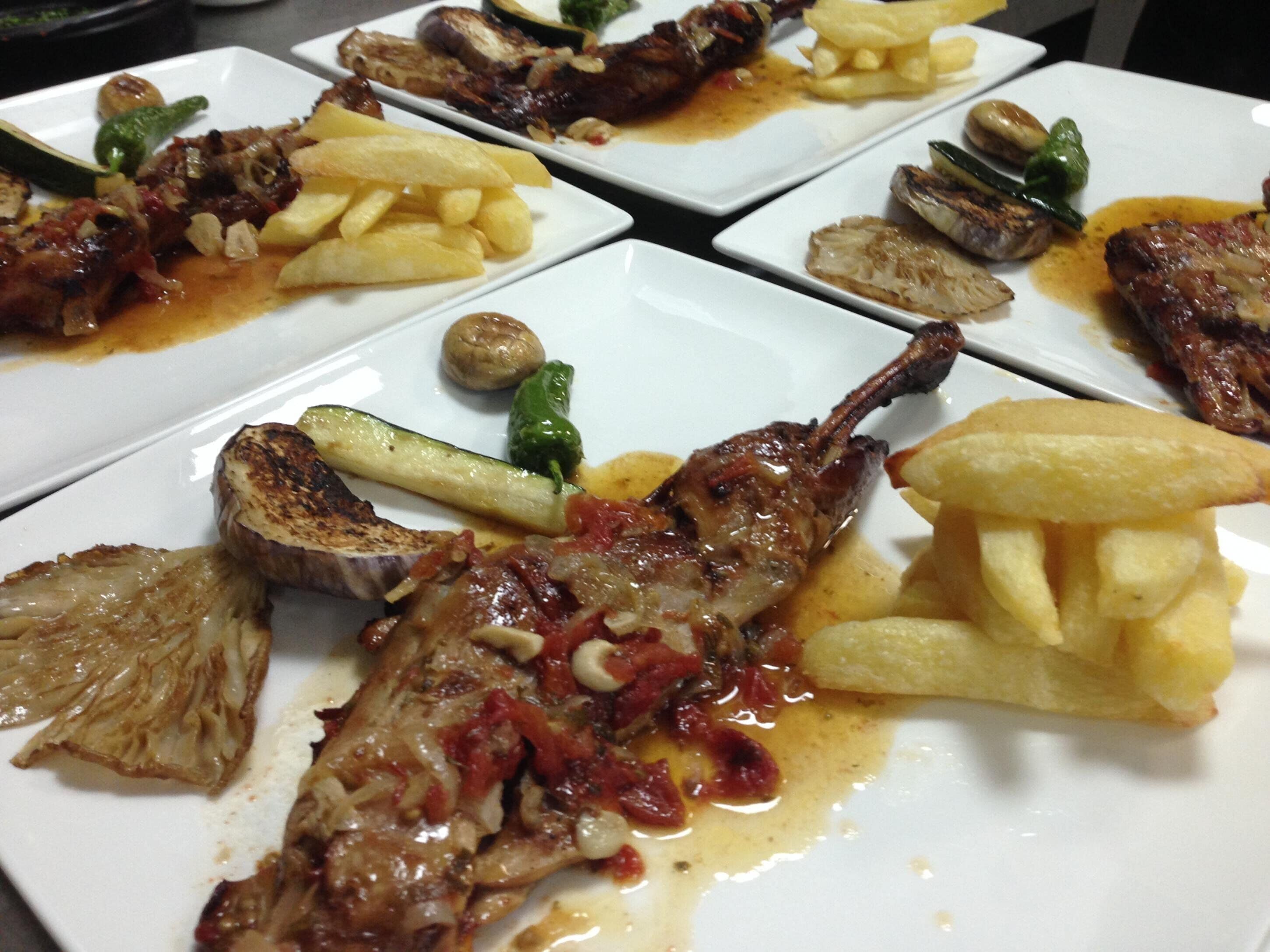A table with multiple square plates of food, including grilled meat, potatoes, and vegetables.