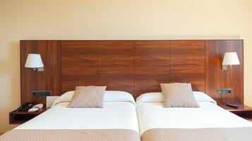 Habitación de hotel con dos camas, cada una con cabecero de madera, lámparas de noche y una mesita con teléfono y control remoto.
