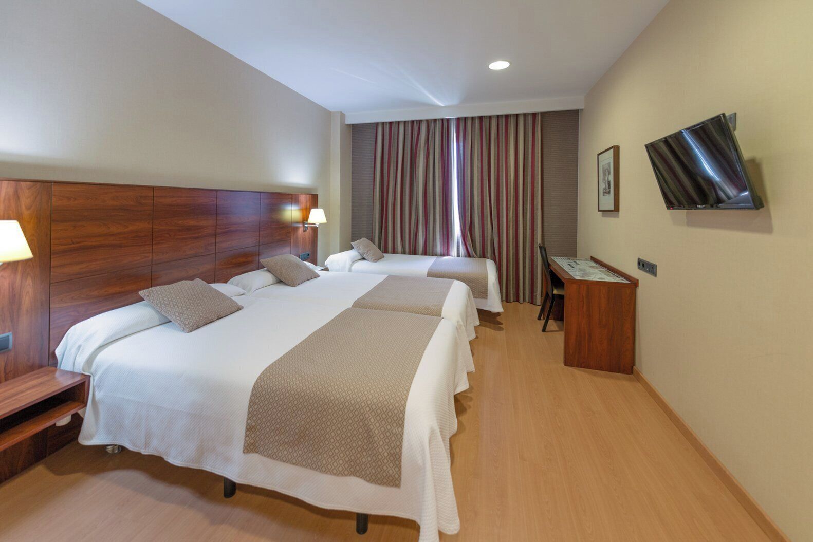 A hotel room with two beds, a desk, a chair, a TV, and a window with curtains.