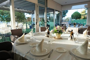 A restaurant table set with white tablecloths, plates, cutlery, and a centerpiece of flowers. - Sercotel Riscal (Puerto Lumbreras)