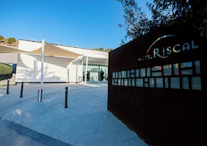 A modern hotel entrance with a clear sky, a distinctive building facade, and a sign reading 'RISCAL HOTEL'. - Sercotel Riscal (Puerto Lumbreras)