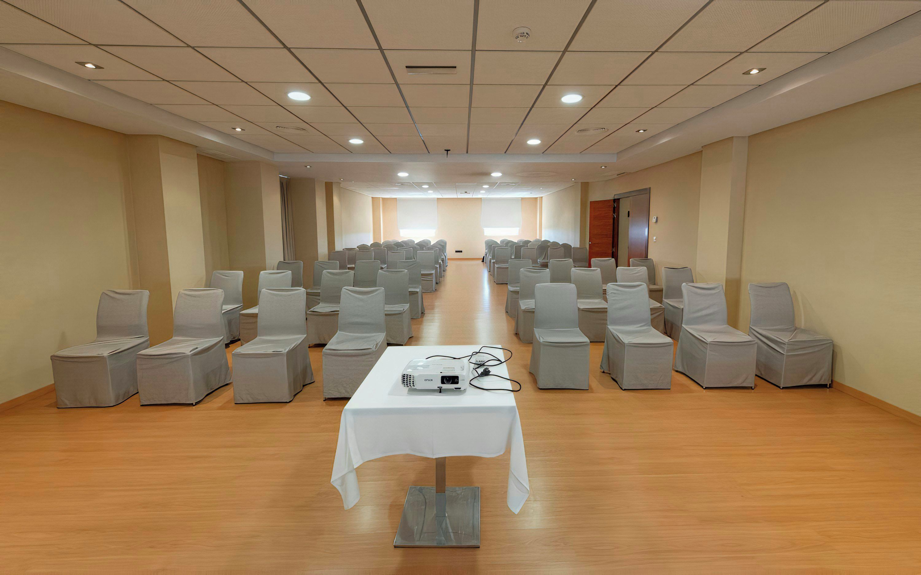 A conference room with rows of chairs, a projector on a table, and a wooden floor.