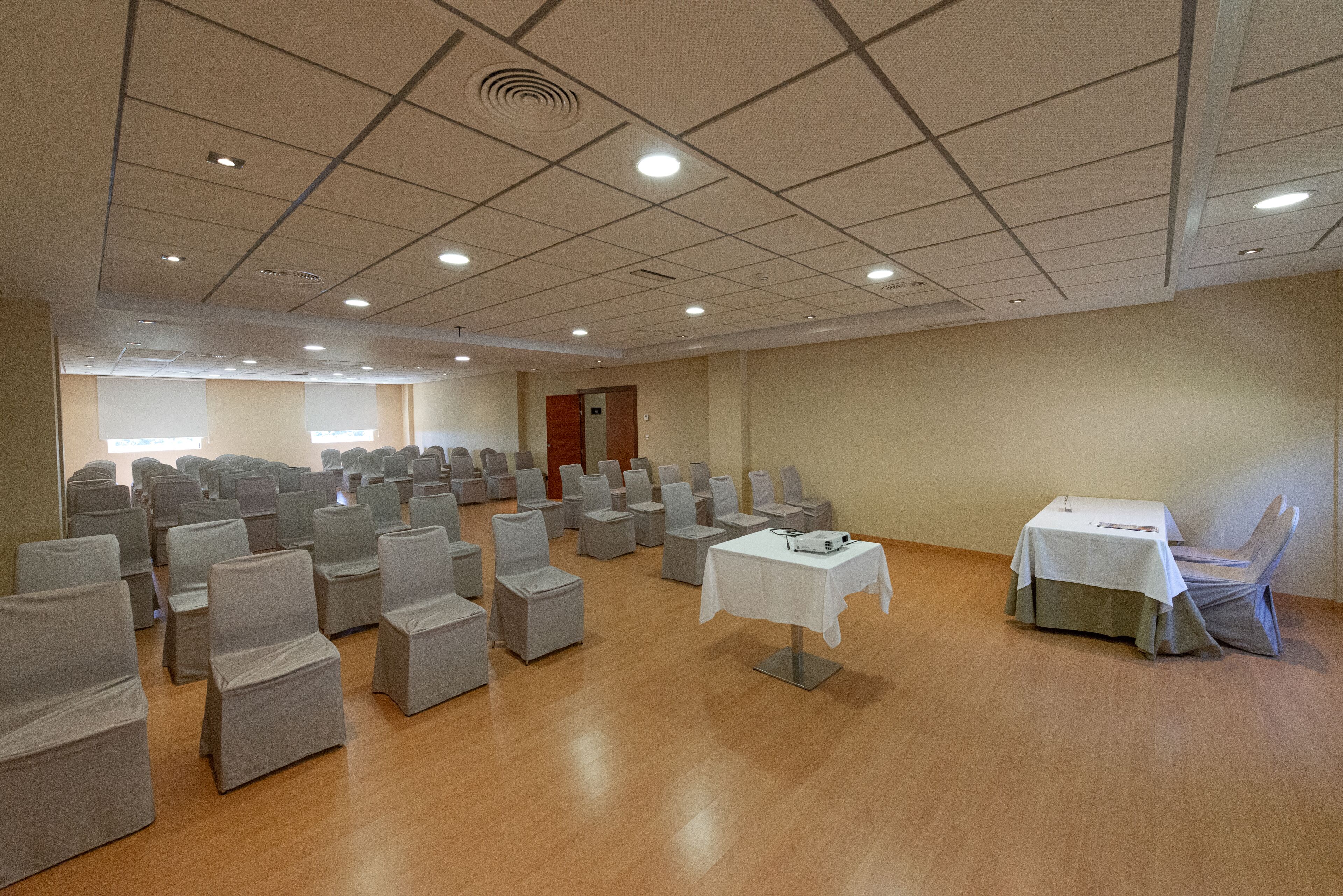 Ein Konferenzraum mit Tischen und Stuhlreihen, Holzböden und einer Decke mit eingelassenen Leuchten.