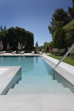 Piscina con sillas de descanso y sombrillas, rodeada de árboles.