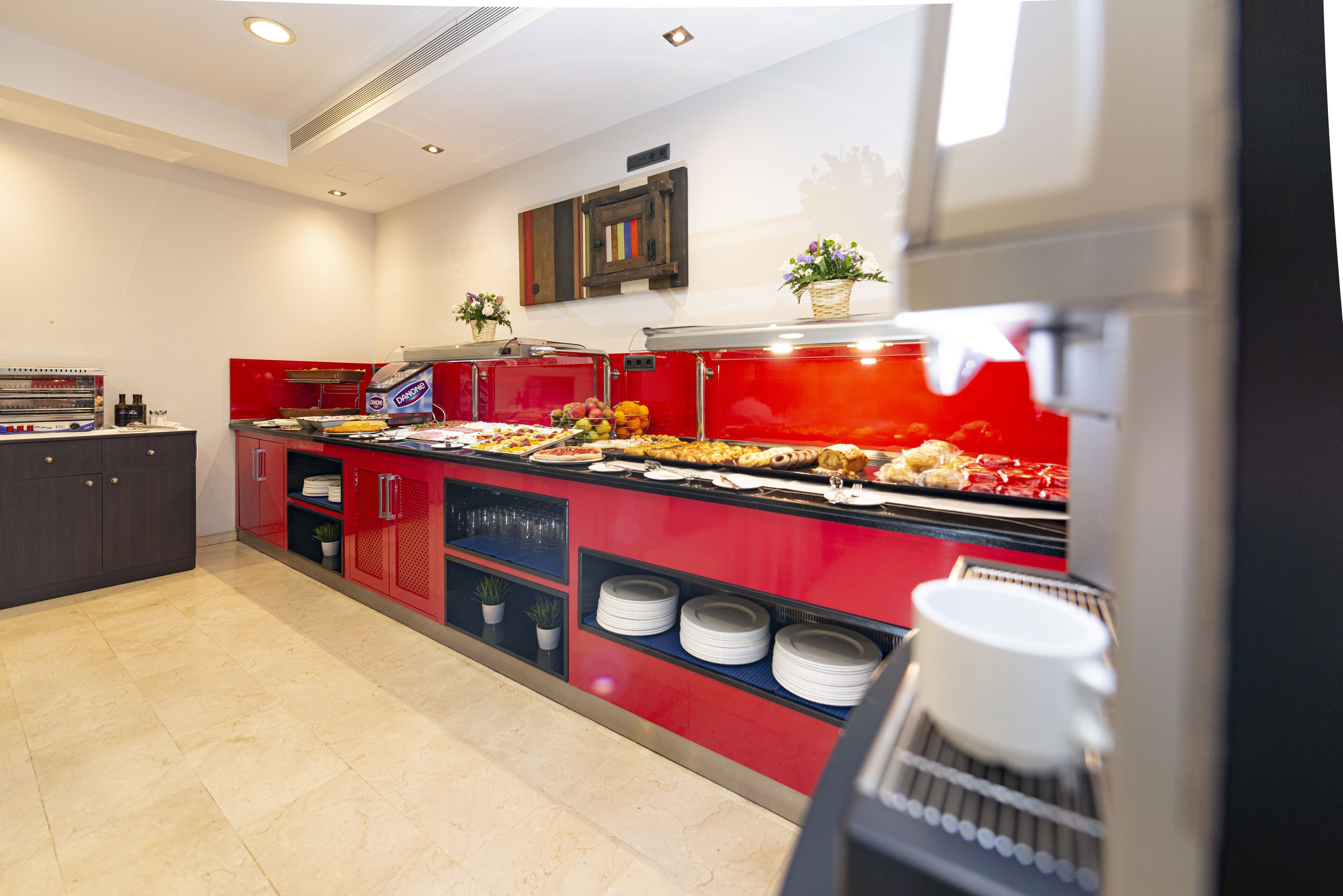 Zona de buffet con un mostrador rojo, diferentes alimentos y una máquina de café.