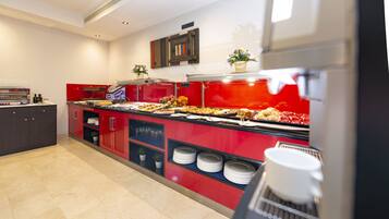 Zona de buffet con un mostrador rojo, diferentes alimentos y una máquina de café.