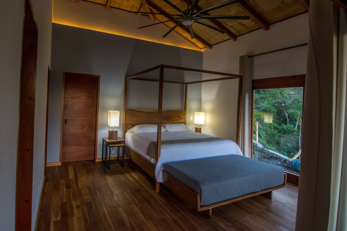 A bedroom with a four-poster bed, wooden flooring, and a sloped ceiling.