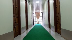 Un largo pasillo con alfombra verde, puertas de madera y una lámpara de techo brillante.