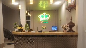 Mostrador de recepción de hotel con logotipo de una corona, cartel de recepción y plantas decorativas.
