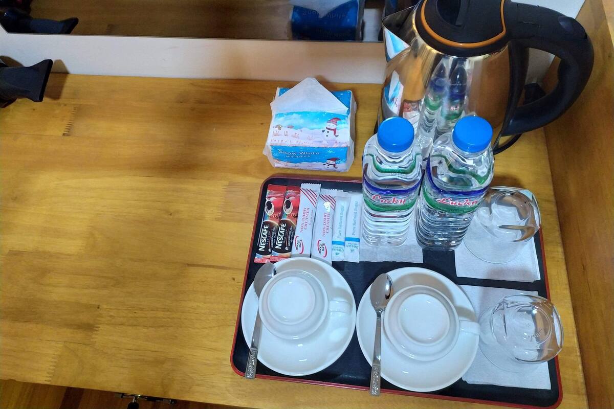 Una mesa de madera con una bandeja que contiene una cafetera, dos botellas de agua, una caja de Nescafé, una cuchara y dos tazas blancas.