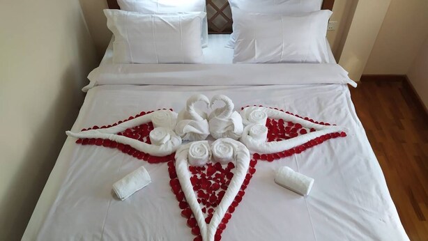 Una cama bien hecha con sábanas blancas y una composición decorativa de pétalos de rosa roja y toallas blancas.