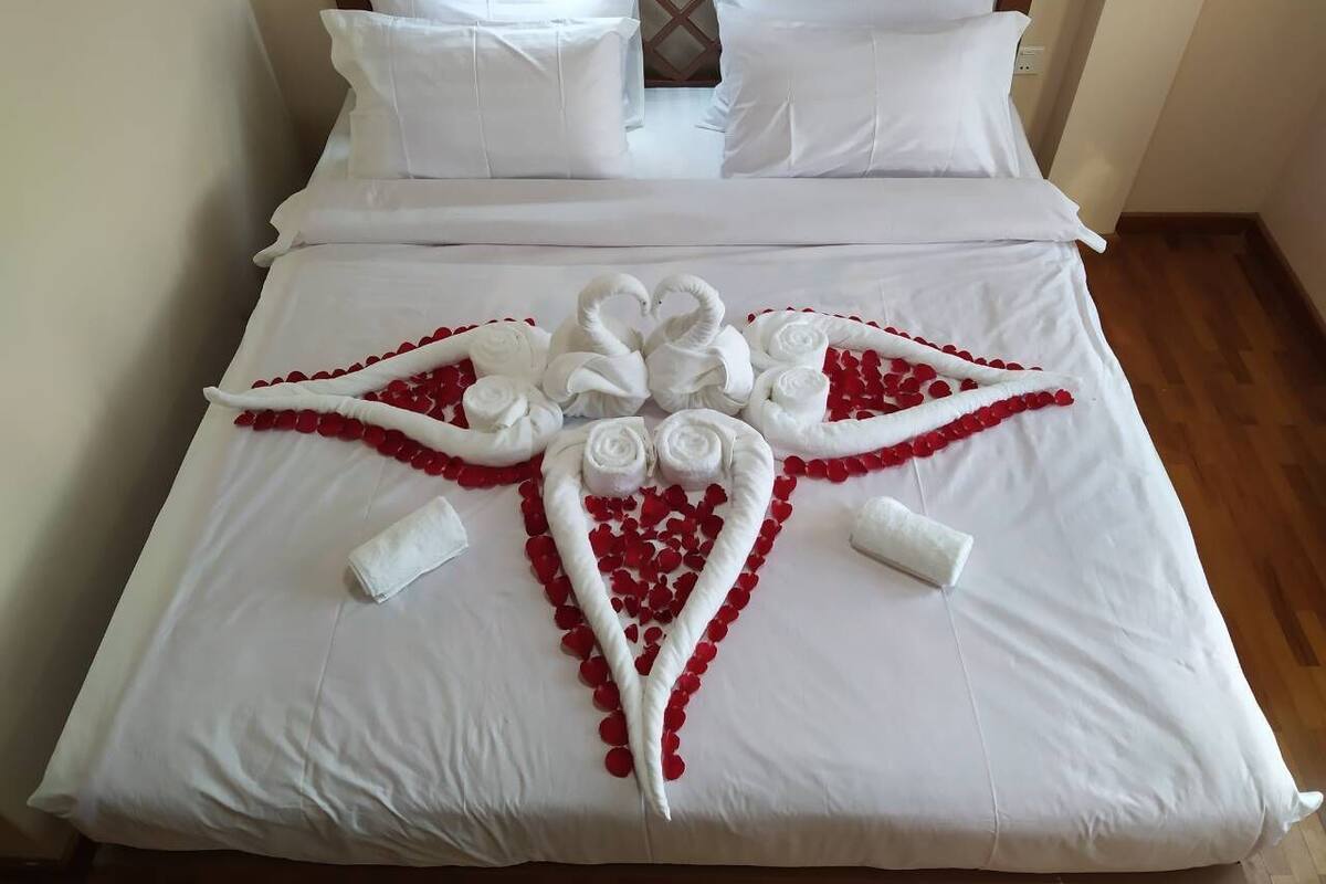 Una cama bien hecha con sábanas blancas y una composición decorativa de pétalos de rosa roja y toallas blancas.