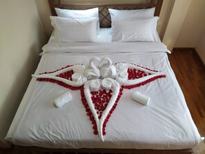 A neatly made bed with white linens and a decorative arrangement of red rose petals and white towels. - Hotel Crown (Pyin Oo Lwin)