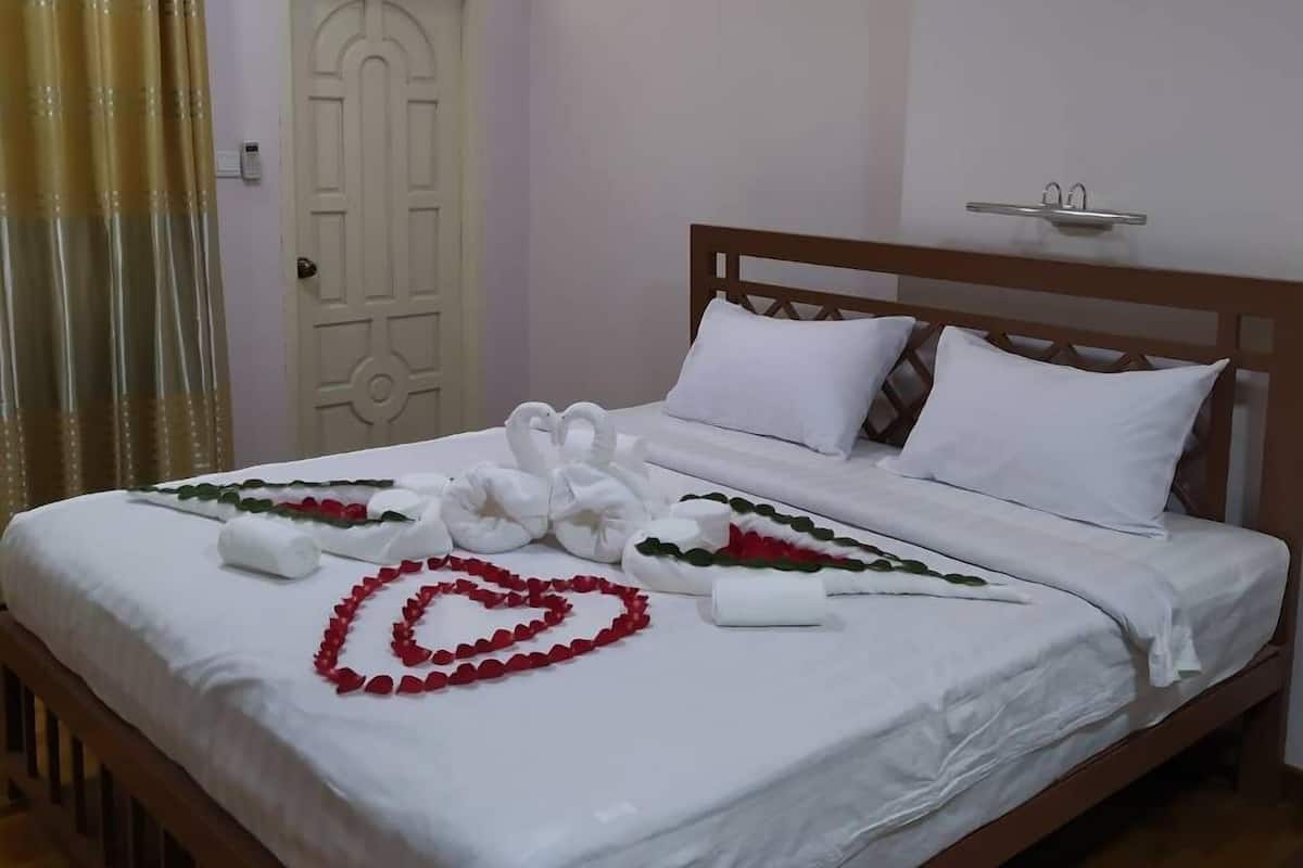 Una cama bien hecha con sábanas blancas y arreglos decorativos de flores rojas y verdes en forma de corazón.