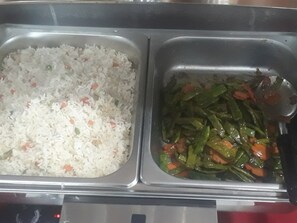 A stainless steel food serving tray with two compartments. One contains white rice with small bits of vegetables, and the other has green beans with carrots.