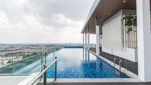 A rooftop infinity pool with a glass balustrade, a wooden deck, and a city view. - MaxStays - Max Home at Da Men Residences (Subang Jaya)