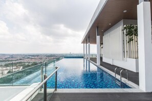 A rooftop infinity pool with a glass balustrade, a wooden deck, and a city view. - MaxStays - Max Home at Da Men Residences (Subang Jaya)