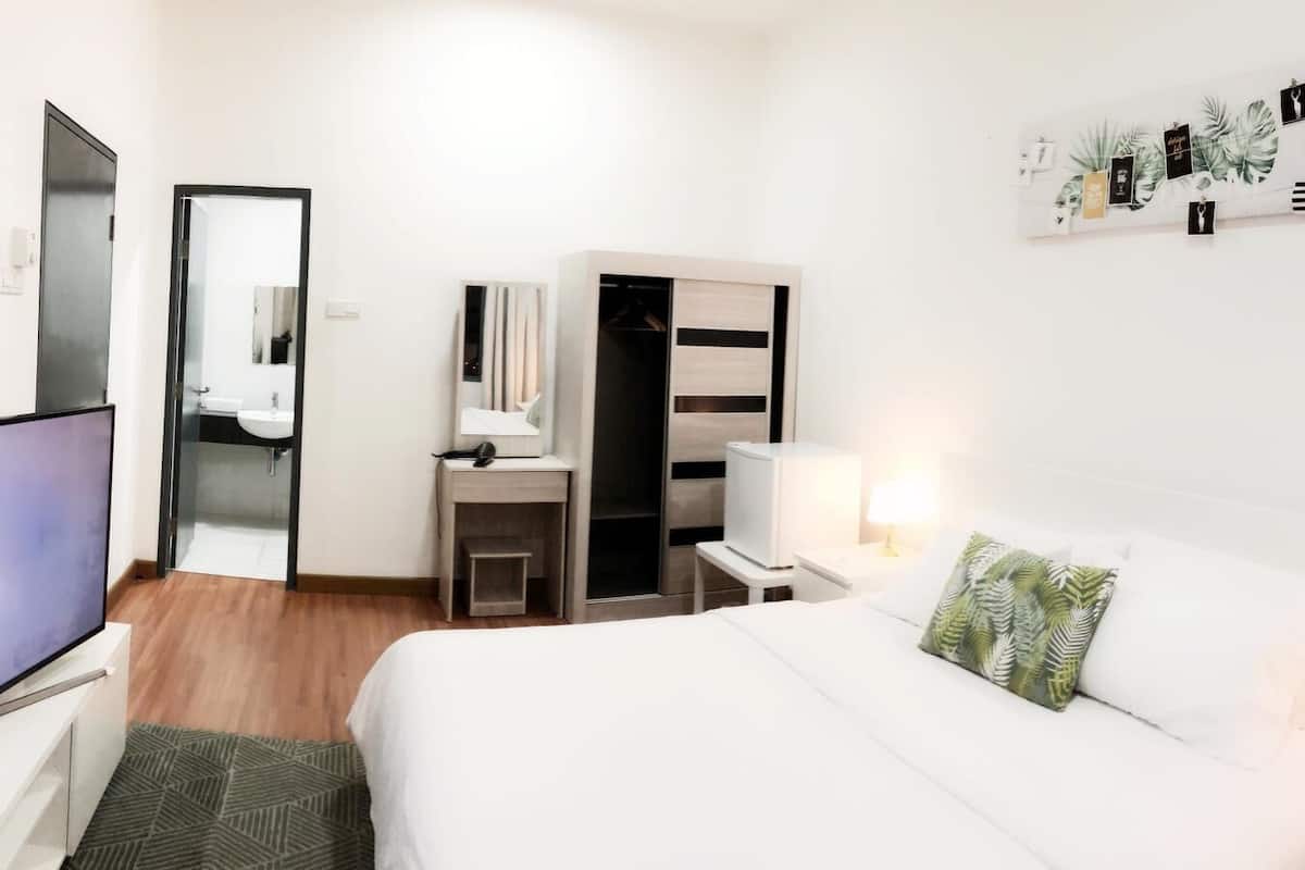 A hotel room with a bed, a TV, a desk with a chair, a wardrobe, and a mirror.
