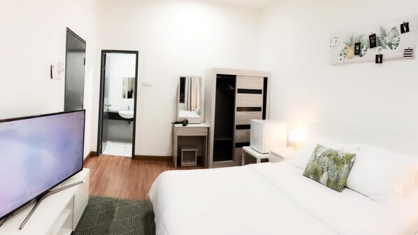 A hotel room with a bed, a TV, a desk with a chair, a wardrobe, and a mirror.