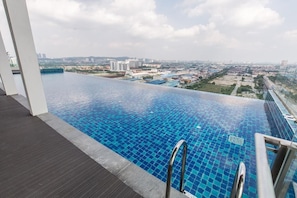 An infinity pool with a city view, a wooden deck, and a metal ladder.