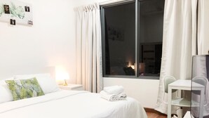 A hotel room with a bed, a desk, a chair, a window with curtains, and a night view outside. - MaxStays - Max Home at Da Men Residences (Subang Jaya)
