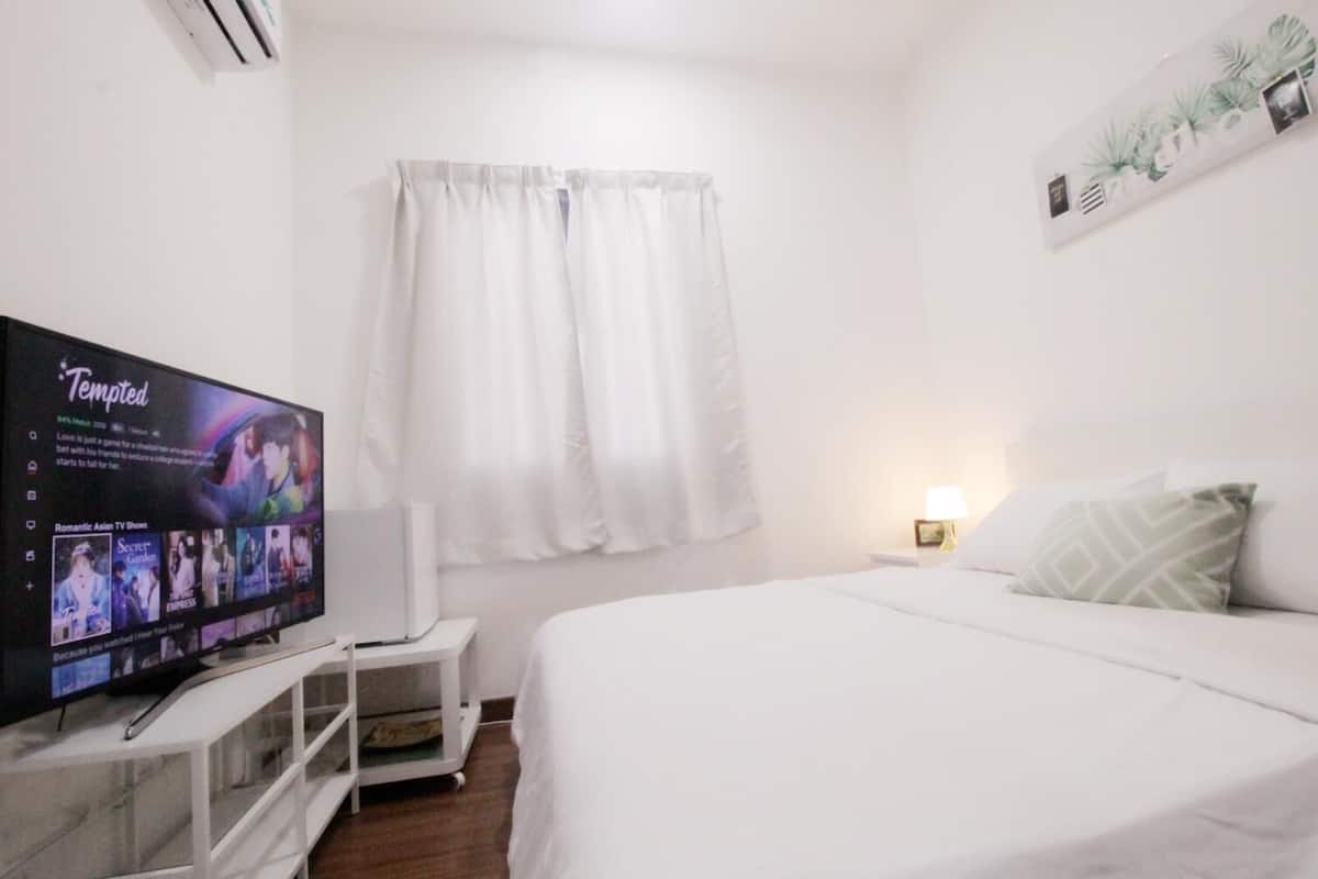 A bedroom with a bed, a TV on a stand, a nightstand, and a wall-mounted plant.