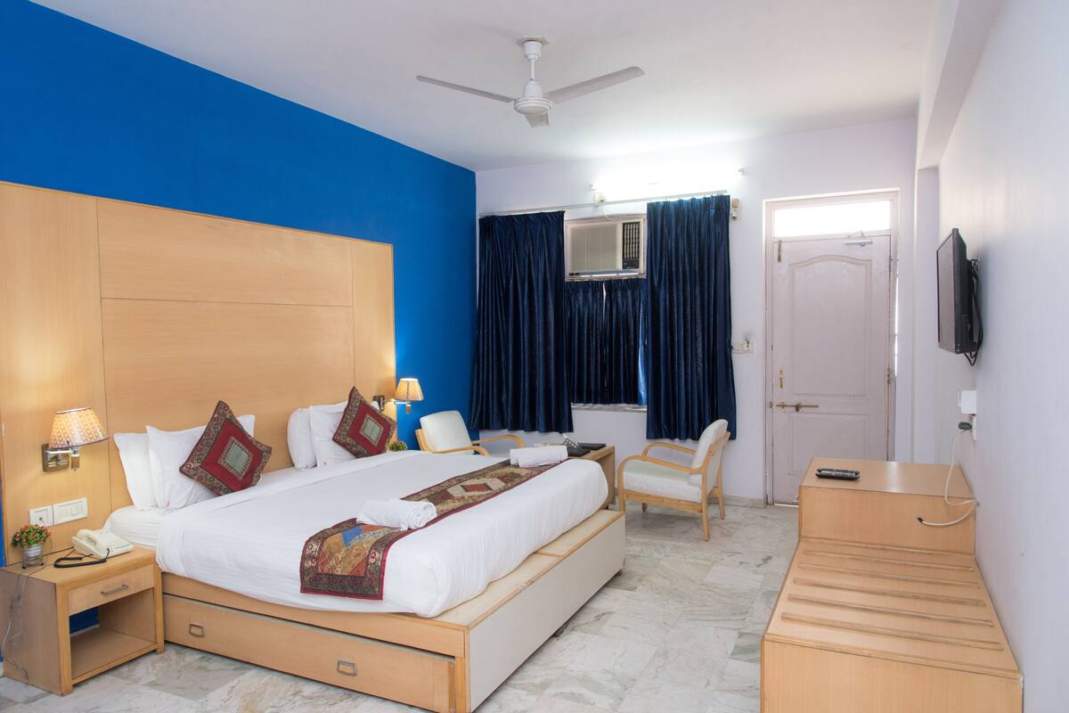 A hotel room with a large bed, a desk, a chair, a wardrobe, a ceiling fan, and a TV.