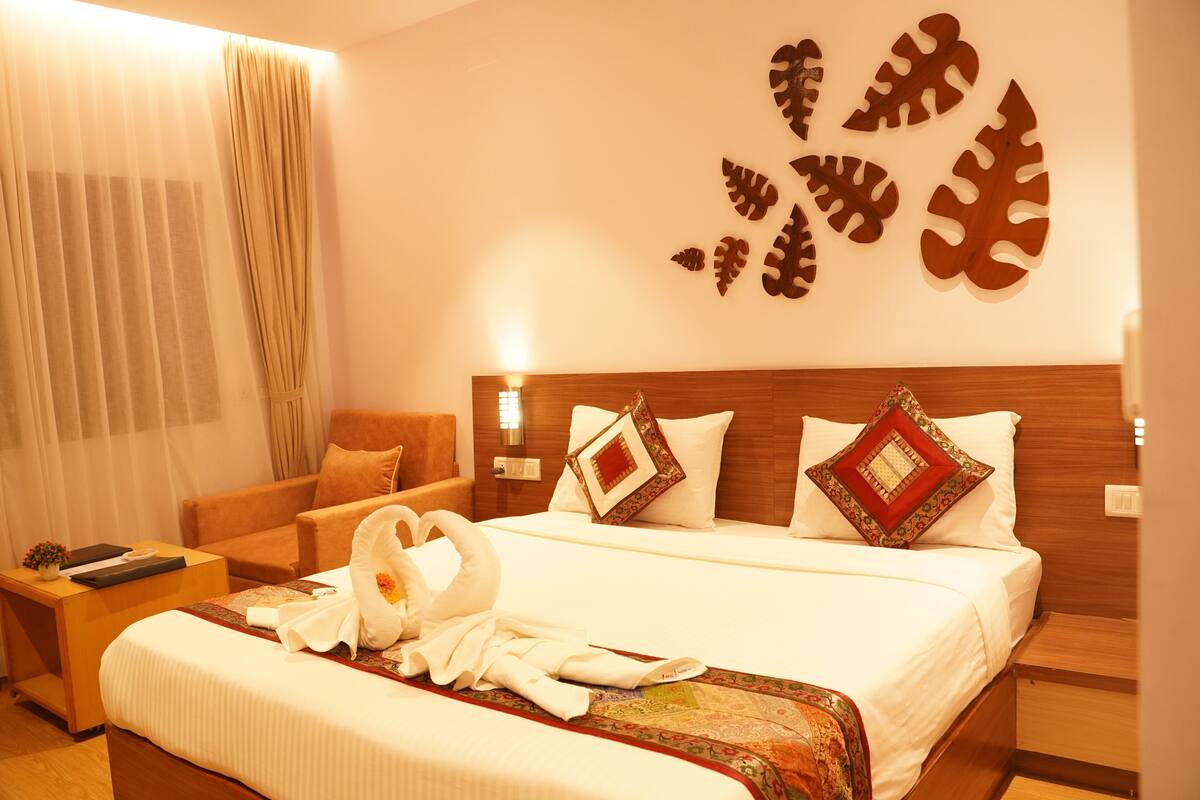 A hotel room with a bed, a nightstand, a chair, and a wall with leaf-shaped decorations.