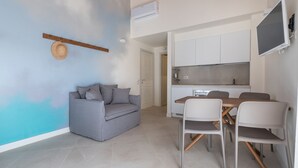 Ein modernes Wohnzimmer mit grauem Sofa, einem Esstisch mit Stühlen und einer Küchenzeile mit Schränken und einem Fernseher.