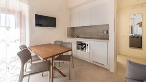 Un espace de vie compact comprenant un coin cuisine, un coin repas avec une table et des chaises en bois, et un coin salon avec un canapé.