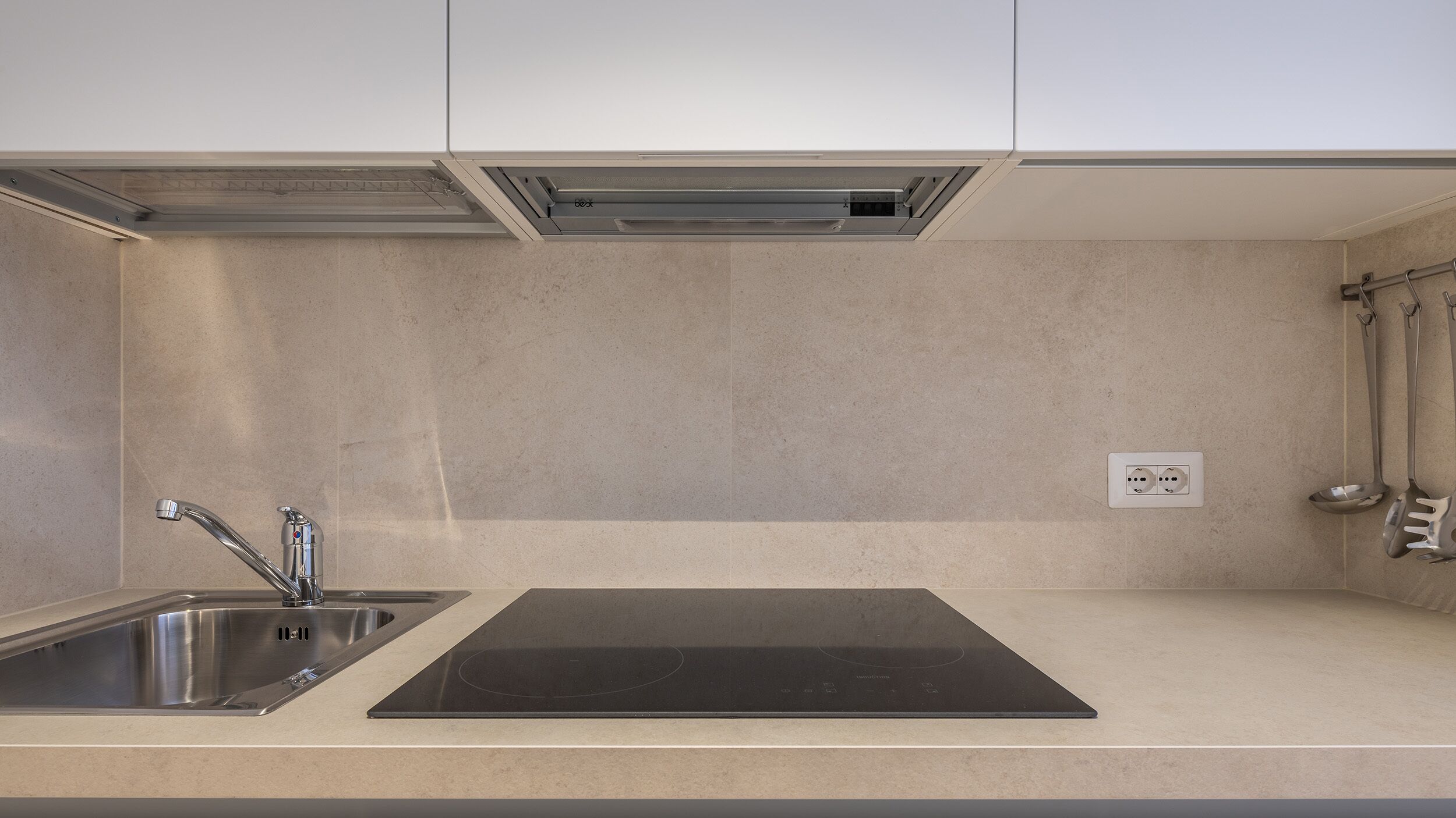 A kitchen with a stainless steel sink, a black induction cooktop, and a wall-mounted oven.