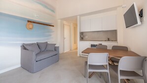 A compact living space with a grey sofa, a wooden dining table, and a kitchenette.
