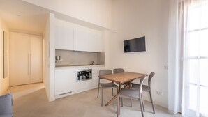 A modern kitchen with white cabinets, a built-in oven, and a dining area with a wooden table and metal chairs.