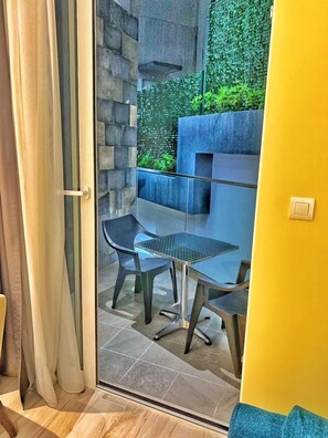 A modern outdoor seating area with a glass partition, a stone wall, and a planter with greenery. - Hotel Pierina (Budva)